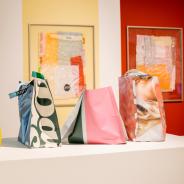 Vinyl bags sit on a pedestal with colorful plastic collages behind them.