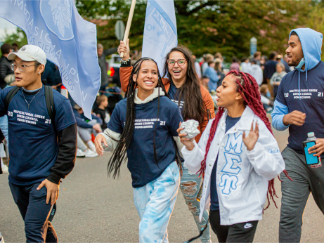 Students wearing Greek letters walking in the Homecoming parade.