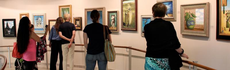 A group of 6 people looking closely at reproductions of popular paintings from the Surrealist movement.