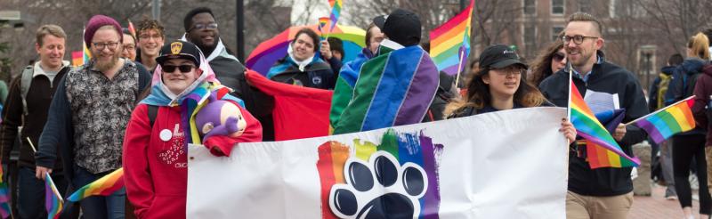 Students and staff marching with a banner that reads LGBTQA Student Resource Center
