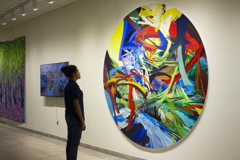 One person looking at a colorful abstract painting larger than themselves.