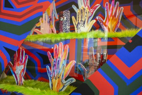 A colorful installation in wall case of hands, print, and a figure with eyes.