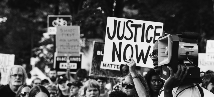 A 'Justice Now' sign is held above the crowd at a protest rally