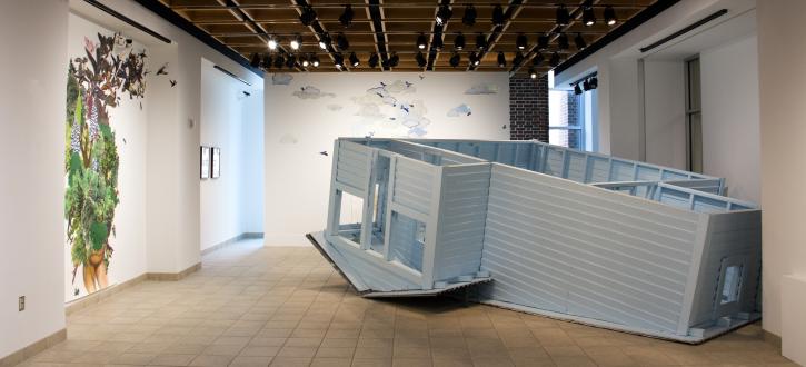 An upside down quarter scaled house in HUB Gallery with large wall collages